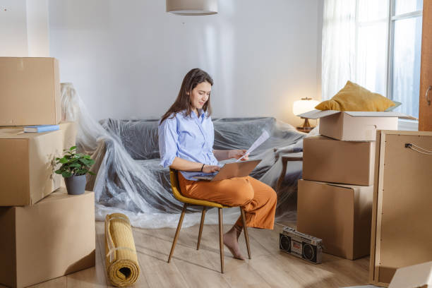 istock Young woman using laptop in new home and holding documents 2148320934