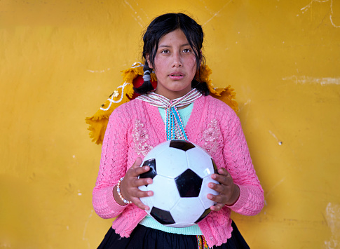 Portrait with yellow background of a girl soccer player from the Quechua ethnic group with the ball in her hands