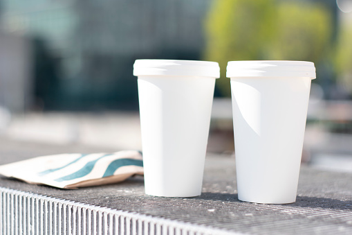 Two white paper cup for hot coffee,Take away, hot beverage coffee cup ,close up two take away coffee,Paper cup of coffee with blurred background of nature and sun
