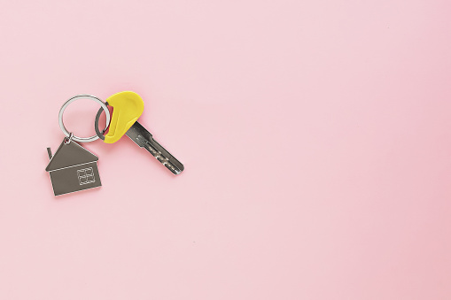 one key with house keychain on a pink background, place for text.