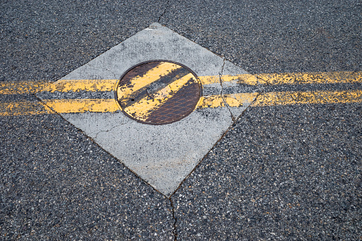 Double yellow lane lines crossing a utility access cover in the middle of a road.