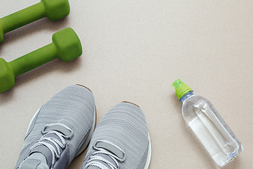 flat lay on the topic of online sports in quarantine, gray sneakers, green dumbbells and a bottle of water