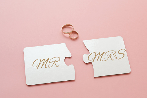 two white disconnected puzzles with the inscription Mr. and Mrs. and two gold wedding rings on a pink background