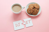 two white disconnected puzzles with the inscription diet, a cup of coffee and a plate with cookies.