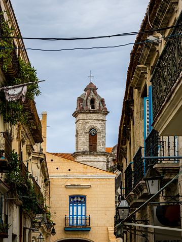 Gazing down San Ignacio street, the baroque bell tower of Havana Cathedral stands as a symbol of Cuba's past, adorned by ornate balconies, offering a view of Old Havana heritage on a overcast day.