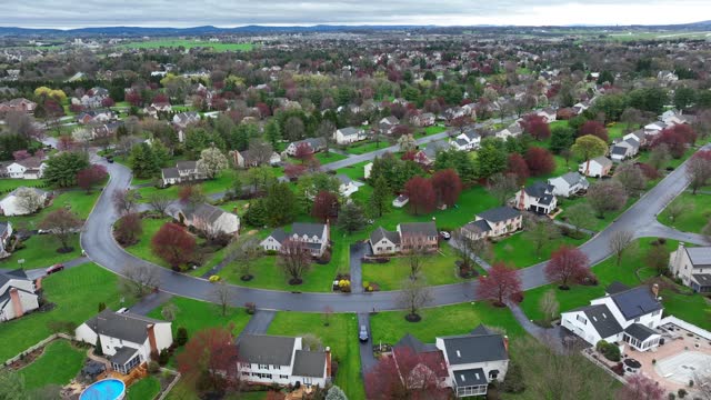 Aerial view of residential houses at spring season. Establishing shot of american neighborhood, suburb. Real estate from above. Colorful trees and grass after rain. Drone orbiting top down.