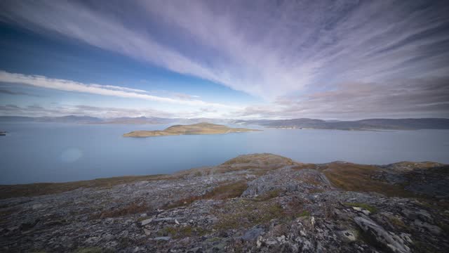 Rocky coast of the fjord with scarce vegetation. Thin clouds carried by the strong wind. Timelapse video.