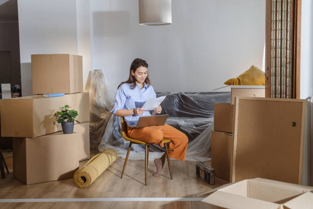 istock Young woman using laptop in new home and holding documents 2148327668
