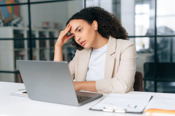 Upset frustrated latino or hispanic curly haired business woman, corporate financial manager, sits in a modern office, sadly looking at a laptop screen, reading bad news, received bad financial report Upset frustrated latino or hispanic curly haired business woman, corporate financial manager, sits in a modern office, sadly looking at a laptop screen, reading bad news, received bad financial report best staffing agency stock pictures, royalty-free photos & images