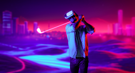 Caucasian man playing golf in metaverse while wearing VR goggles to enter simulated virtual world. Handsome gamer using virtual reality glasses enter in neon golf course. Innovation. Sport. Deviation.