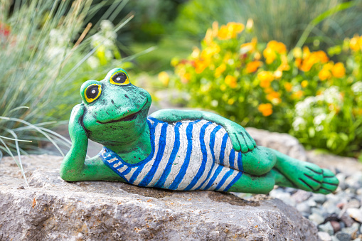 Garden sculpture of frog lying on flowerbed