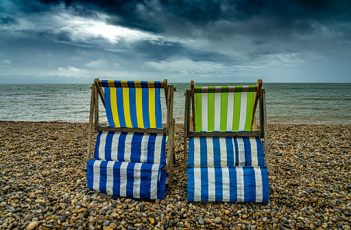 Two deck chairs alone on a beach on a cloudy stormy day