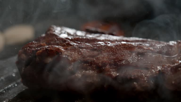 cook presses a juicy piece of beef to a hot frying pan with tongs