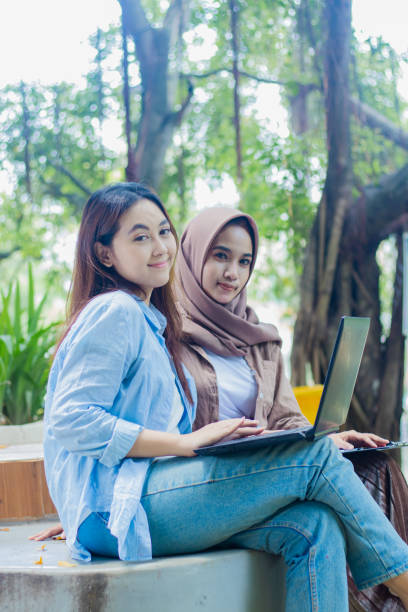 istock Two Asian women smiling gracefully at the camera chatting about something while holding laptops, pens, books and clipboards in the campus park. female students for promotion and lifestyle concepts 2148329301