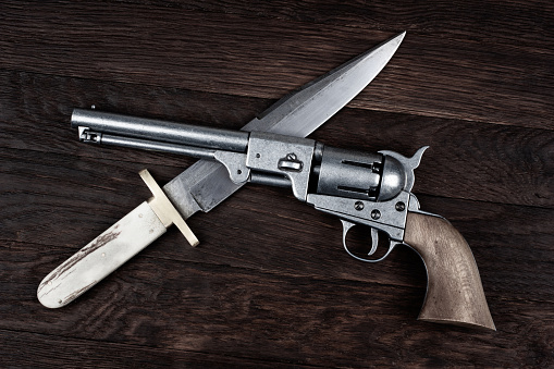Old West Revolver with bowie knife on wooden deck background.
