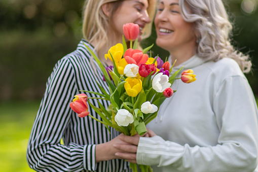 Daughter hugs mother, focus on tulip bouquet.