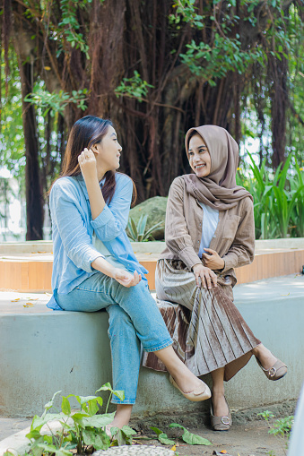 The two Asian women interact with happy smiles chatting in the campus park. student for the concept of human interest and lifestyle