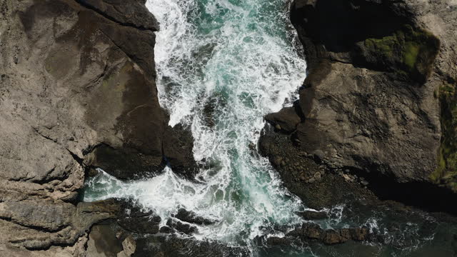 White foamy waves relentlessly flow into a narrow cove and break against rocks