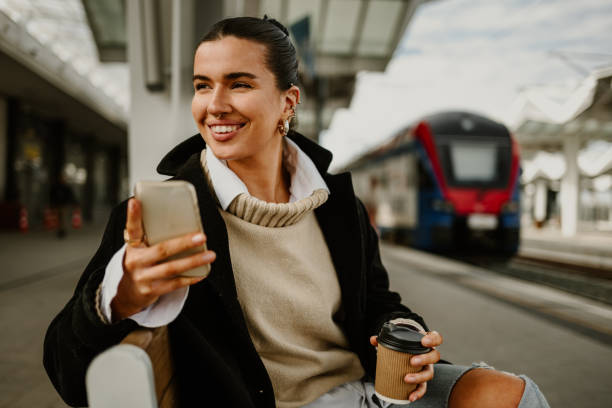 istock Smiling young woman sitting on a train station with cellphone in hands 2148332279