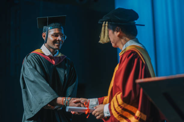 istock Asian Indian university student hand shake with dean receiving diploma in auditorium during graduation ceremony event 2148332481