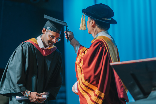 Asian Malay Dean performing the turning of the tassel for Indian university student during convocation ceremony on stage