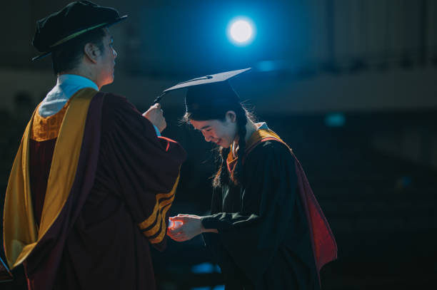 Convocation ceremony Asian Graduation university students bowing receiving paper scroll from Dean standing on Auditorium stage