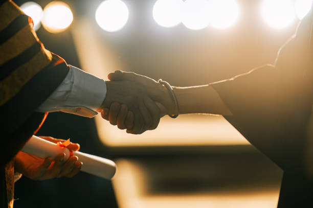 close up Convocation ceremony Asian Dean handshake Graduation university student handover graduation scroll on auditorium stage