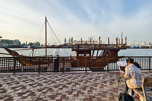 girl artist paints an old wooden ship on the embankment in Sharjah. Sharjah. United Arab Emirates, January 28, 2024.