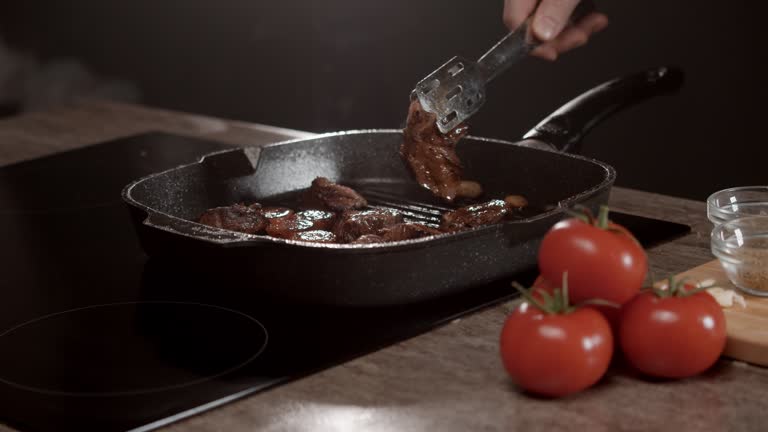 The chef turns over the pieces of beef that have been fried in a black grill pan.