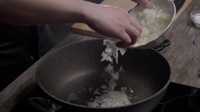 Cook pours oil into a pan and adds sliced onions.