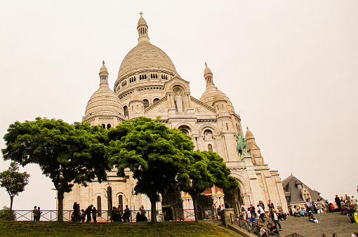 The white domed church in the iconic district of Montmartre. Tourists visit the basilica in a grey day of summer.