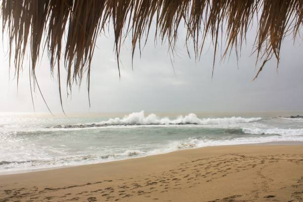 istock A tranquil sandy beach with a charming straw-roofed beach hut nestled under moody, cloud-filled skies. 2148334323