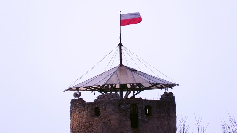 A stone tower with a Polish flag flying at the top in a strong wind