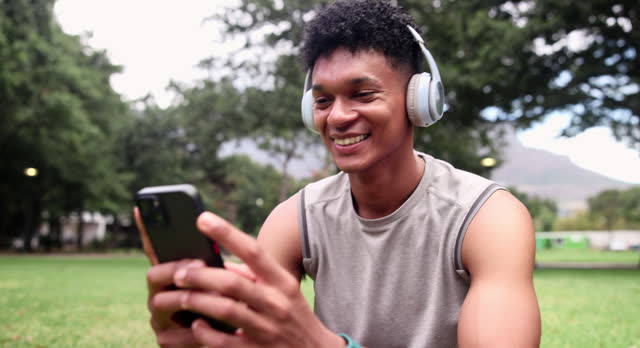 Fitness, phone and happy man with headphones at park on break for streaming music at garden in summer. Sports, smartphone and person listening to radio, typing or laughing at meme on social media