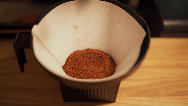 Close-up of male hands pouring ground coffee into a disposable paper filter for a coffee machine