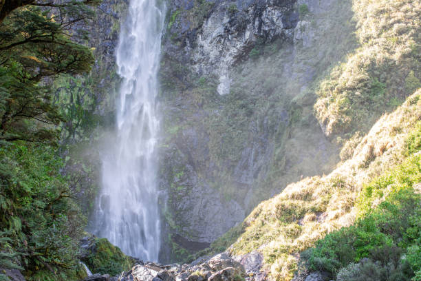 istock Sunlit waterfall cascades through lush NZ foliage, a serene Arthur's Pass gem 2148336314