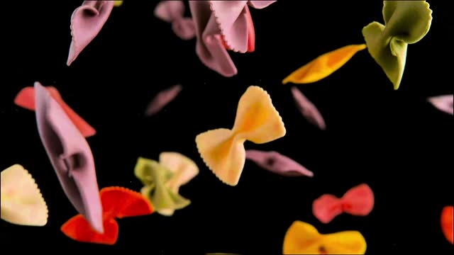 Colorful pasta in the shape of bows flies in the air in slow motion. Popular pasta suitable for many dishes. A food product that is made from unleavened and chemically leavened dough