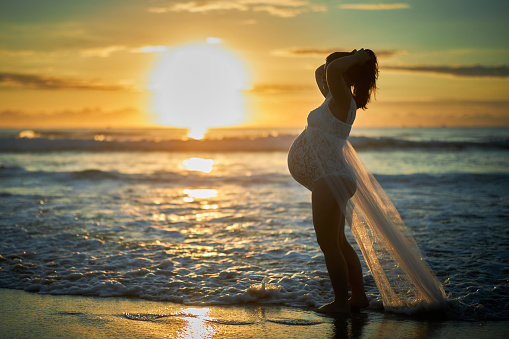 Maternity sunrise showing belly abdomen with baby birth due soon. Sunrise pregnancy waves ocean and sandy shorefront at dawn.