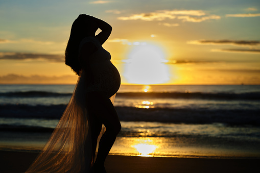 Maternity sunrise showing belly abdomen with baby birth due soon. Sunrise pregnancy waves ocean and sandy shorefront at dawn.