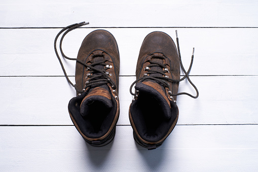 A pair of brown hiking boots is placed on top of a white wooden floor.