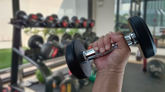 Man's hands lifting dumbbells, building arm muscles in the fitness room.