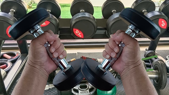 Man's hands lifting dumbbells, building arm muscles in the fitness room.
