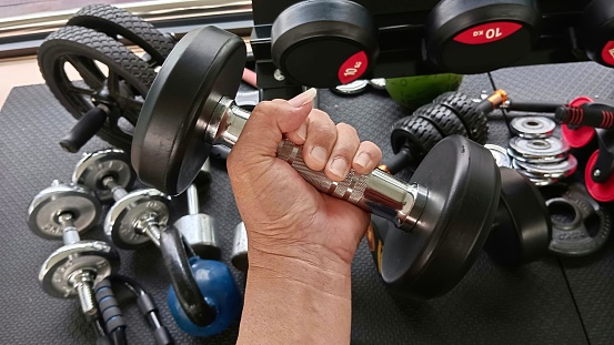 Man's hands lifting dumbbells, building arm muscles in the fitness room.