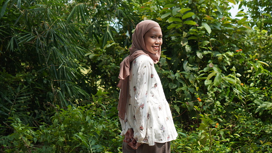 pausing in the bushes to take photos. A beautiful woman wearing a brown hijab and white robe with floral patterns looks happy