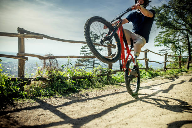 A male mountain bike rider does a no-hander off a jump in a dirt jump park.