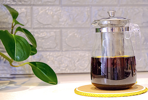 A glass teapot with brewed black tea is in the kitchen, close-up.