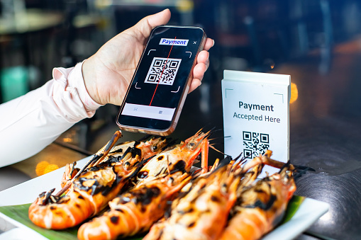 Selective focus to smartphone scan QR code payment tag with blurry grilled river prawns in restaurant to accepted generate digital pay without money. Qr code payment concept.