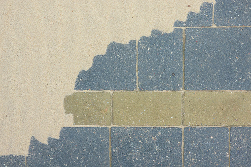 A fragment of a pavement made of gray and green paving slabs is partially covered with sand. Background. Texture.
