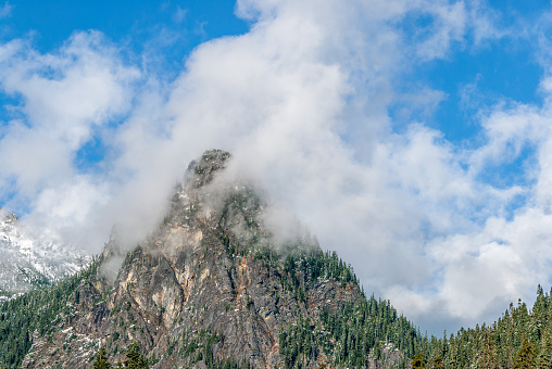 Embraced by cotton candy clouds, majestic Guye Peak stands tall in the Cascade Mountain Range of Washington, basking in the warmth of a sunny day.  This picture of Guye Peak was photographed from Gold Creek in the Mount Baker Snoqualmie National Forest near North Bend, Washington State, USA.