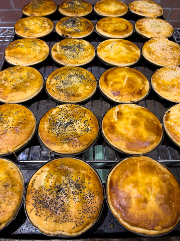 Vertical high angle closeup photo of a variety of golden freshly baked pies, hot out of the wood-fired oven in a Cafe Bakery.